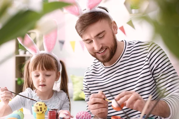 Father painting Easter eggs with his daughter at table