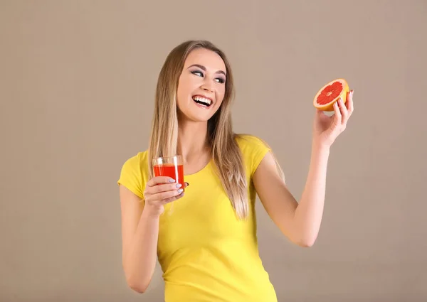 Belle jeune femme avec un verre de jus d'agrumes et de fruits sur fond de couleur — Photo
