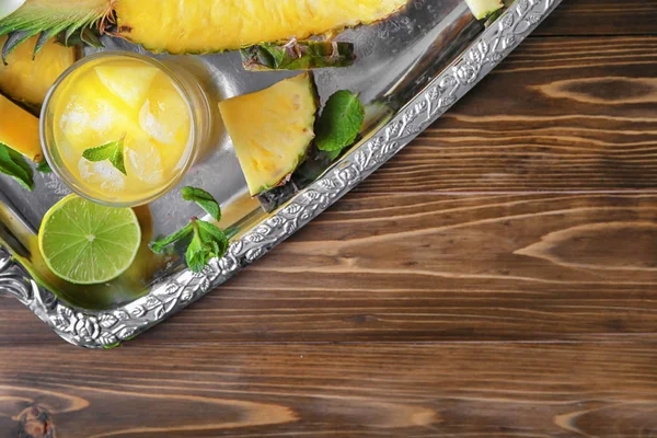 Zásobník s plátky ananasu a sklenici čerstvé šťávy na dřevěný stůl — Stock fotografie