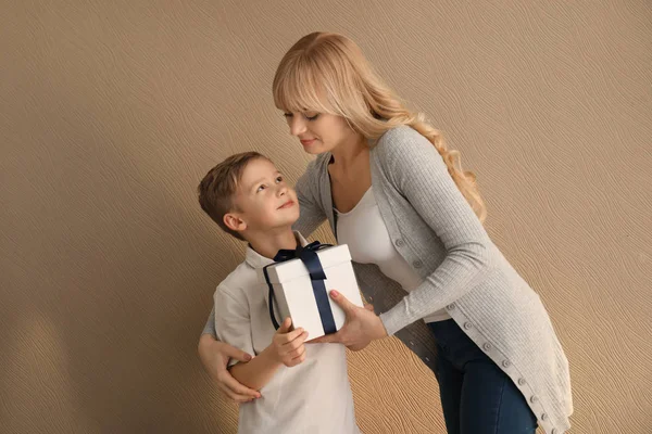 Portrait of cute little boy and his mother with gift box on color background — Stock Photo, Image