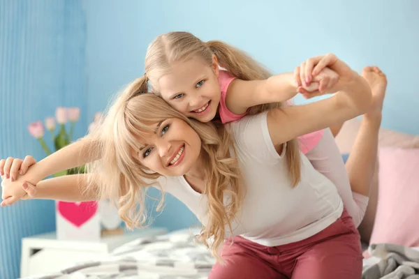 Mujer joven jugando con su hija en el dormitorio — Foto de Stock