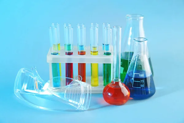 Chemical glassware with colorful samples and lab goggles on color background — Stock Photo, Image