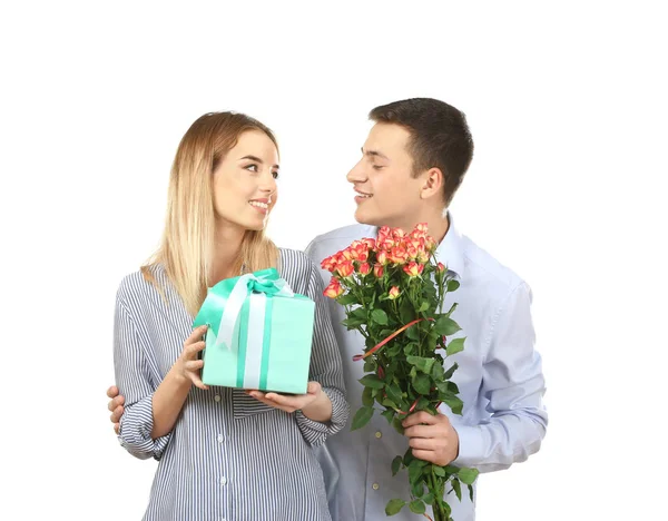 Jovem casal feliz com presente e flores no fundo branco — Fotografia de Stock