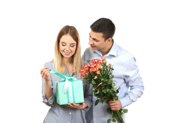 Jovem casal feliz com presente e flores no fundo branco — Fotografia de Stock