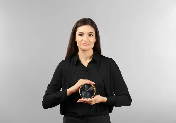 Young businesswoman holding alarm clock on gray background — Stock Photo, Image