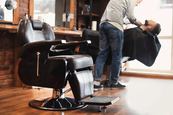 Silla y peluquero profesional trabajando con el cliente en un moderno salón de peluquería — Foto de Stock