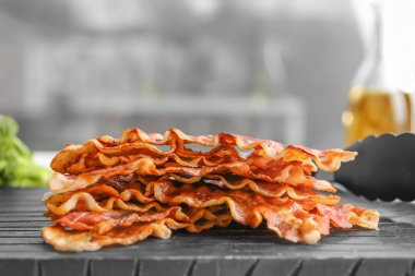 Board with fried bacon rashers on blurred background clipart
