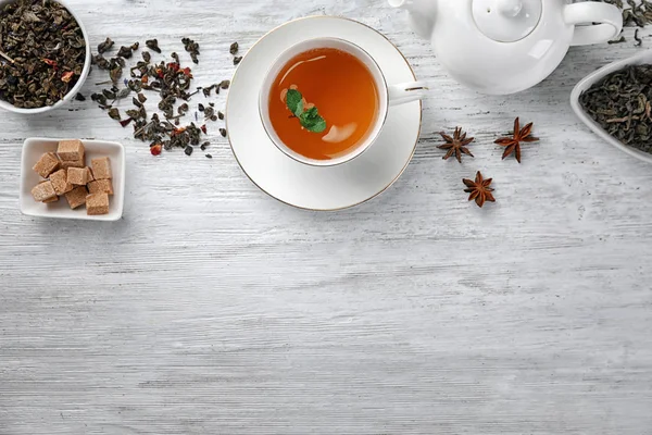 Suché listy zeleného čaje a šálek aromatické nápoje na stole — Stock fotografie