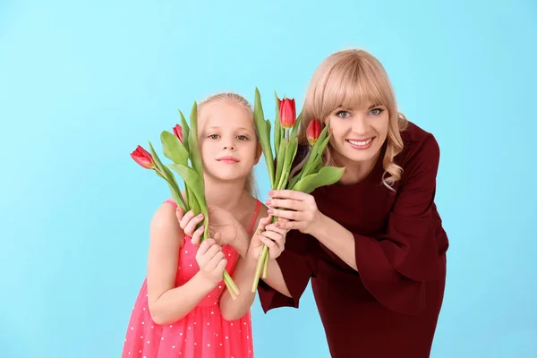 Portrait of cute little girl and her mother with tulips on color background — Stock Photo, Image