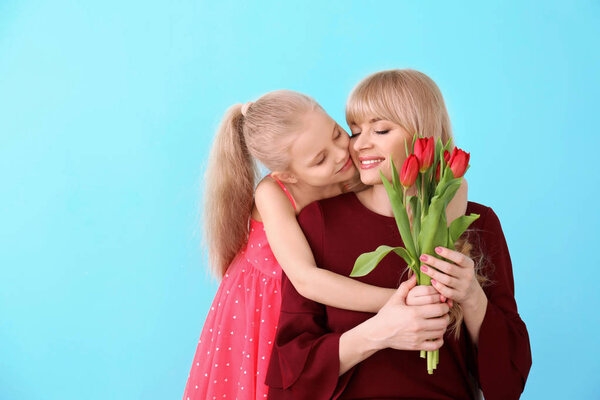 Портрет милой маленькой девочки и ее матери с букетом тюльпанов на цветном фоне
