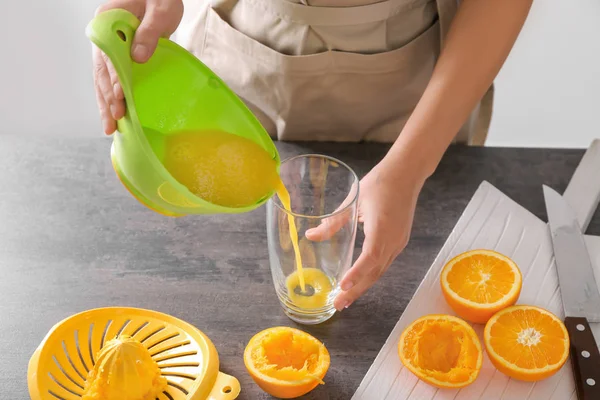 Женщина наливает вкусный цитрусовый сок в стакан на стол — стоковое фото
