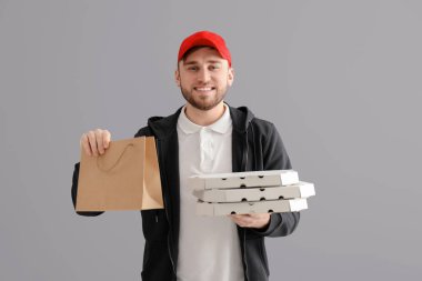 Karton pizza kutuları ve gri arka plan üzerinde kağıt torba olan genç adam. Gıda dağıtım hizmeti