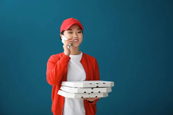 Mulher asiática com caixas de pizza de papelão falando no telefone contra fundo de cor. Serviço de entrega de alimentos — Fotografia de Stock