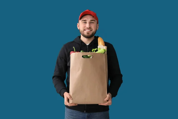 Giovane uomo con prodotti in sacchetto di carta su sfondo a colori. Servizio di consegna cibo — Foto Stock