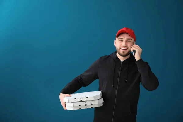 Young man with cardboard pizza boxes talking on phone against color background. Food delivery service — Stock Photo, Image
