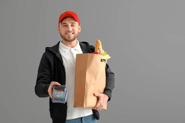 Young man with paper bag and bank terminal on gray background. Food delivery service — Stock Photo, Image