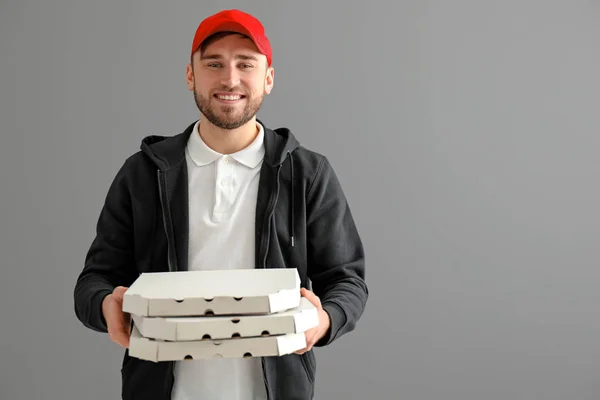 Young man with cardboard pizza boxes on gray background. Food delivery service — Stock Photo, Image