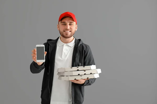 Young man with cardboard pizza boxes and mobile phone on gray background. Food delivery service — Stock Photo, Image