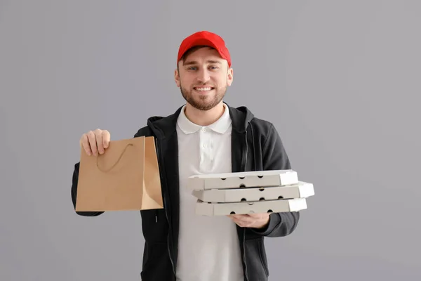 Young man with cardboard pizza boxes and paper bag on gray background. Food delivery service — Stock Photo, Image