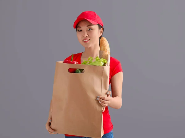 Asian woman with products in paper bag on gray background. Food delivery service — Stock Photo, Image