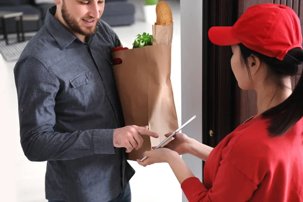 Young man signing on tablet for food delivery at doorway — Stock Photo, Image
