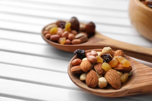 Spoons with different nuts and raisins on wooden table — Stock Photo, Image