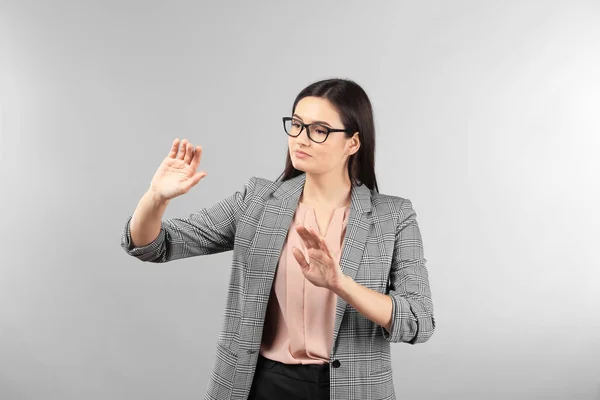 Young businesswoman using virtual screen on gray background — Stock Photo, Image