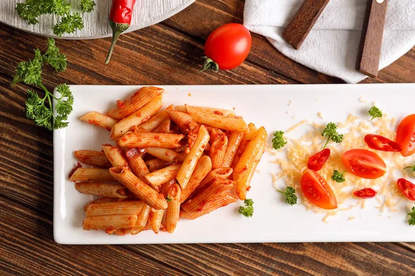 Plaat van smakelijke penne pasta met tomatensaus op houten tafel, bovenaanzicht — Stockfoto