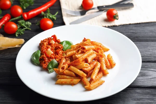 Plate with tasty penne pasta and bolognese sauce on wooden table — Stock Photo, Image