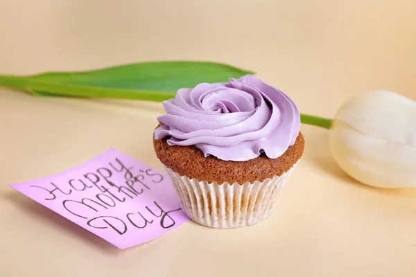 Tarjeta con palabras FELIZ DÍA DE LA MADRE, tulipán blanco y sabroso cupcake en el fondo de color — Foto de Stock
