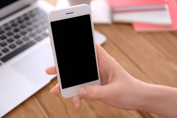 Woman holding smartphone with blank screen at table — Stock Photo, Image