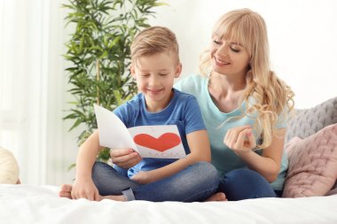 Sevimli küçük çocuk ve annesi yatak odasında el yapımı kart ile portre