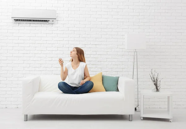 Mladá žena zapnutí klimatizace, zatímco sedí na gauči doma — Stock fotografie