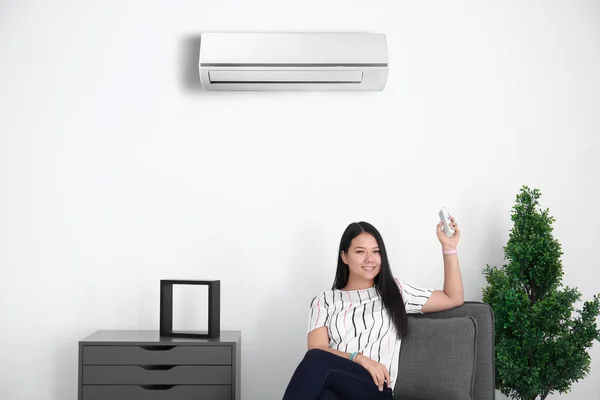 Mujer joven encendiendo el aire acondicionado mientras está sentada en el sillón en casa — Foto de Stock