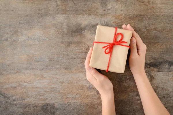 Mujer sosteniendo caja de regalo sobre fondo de madera, vista superior — Foto de Stock