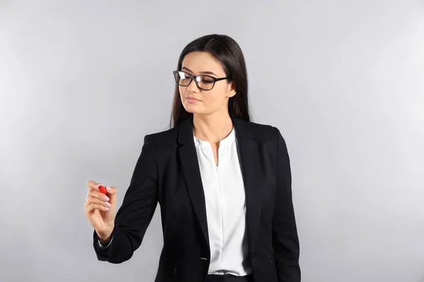 Young businesswoman writing on virtual screen against gray background — Stock Photo, Image