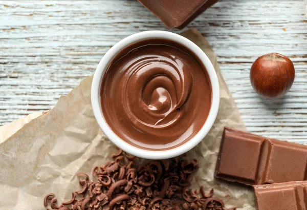 Kom met smakelijk gesmolten chocolade op houten achtergrond — Stockfoto