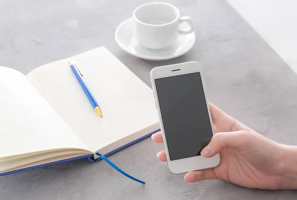 Woman holding smartphone with blank screen at table — Stock Photo, Image