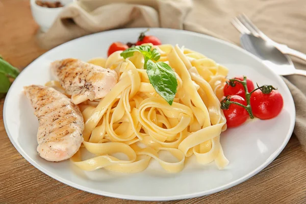 Plate of delicious pasta with grilled chicken fillet and tomatoes on table — Stock Photo, Image