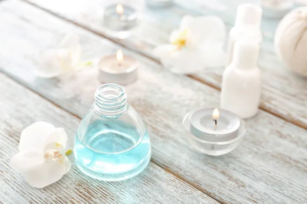 Bottle of essential oil for spa procedures and beautiful flower on wooden table — Stock Photo, Image