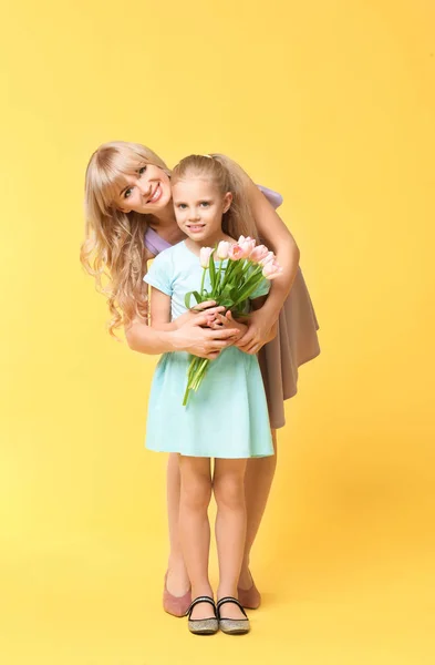 Portrait of cute little girl and her mother with tulip bouquet on color background — Stock Photo, Image