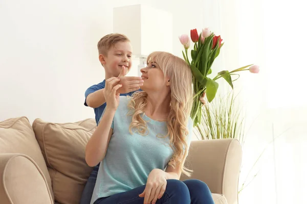 Schattige kleine jongen die zijn moeder met tulip boeket thuis verrassend — Stockfoto