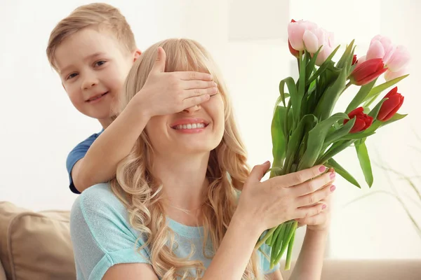 Ładny mały chłopiec, zaskakujące, jego matka z bukiet tulipanów w domu — Zdjęcie stockowe