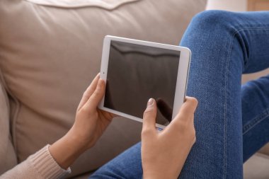 Evde kanepede oturan ise tablet bilgisayar kullanan genç kadın