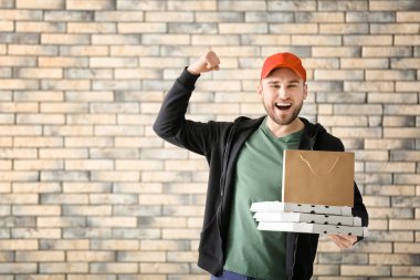 Karton pizza kutuları ve kağıt torba tuğla duvar arka plan üzerinde olan genç adam. Gıda dağıtım hizmeti
