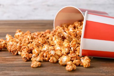 Ahşap masa üzerinde lezzetli karamelli patlamış mısır ile devrilmiş bardak