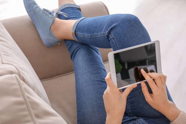 Mujer joven usando tableta mientras descansa en el sofá en casa — Foto de Stock