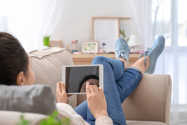 Mujer joven usando tableta mientras descansa en el sofá en casa — Foto de Stock