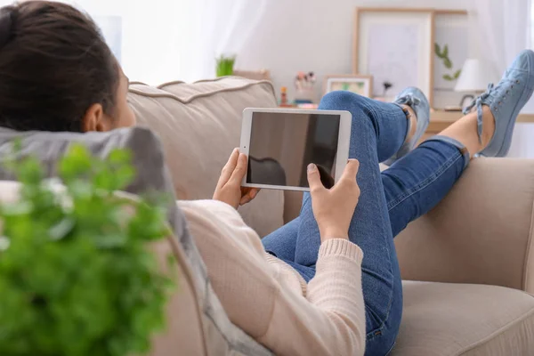 Jeune femme utilisant un ordinateur tablette tout en se reposant sur le canapé à la maison — Photo