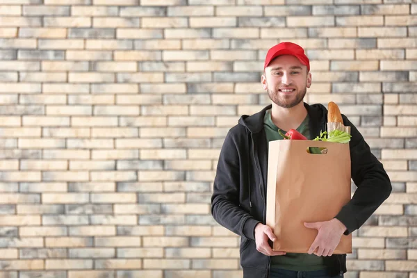 Young man with products in paper bag on brick wall background. Food delivery service — Stock Photo, Image